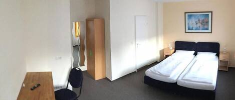 A hotel room with a bed, a desk, a chair, a wardrobe, and a painting on the wall.