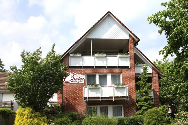 A two-story hotel with a red brick facade, balconies with white railings, and a sign indicating it is a hotel.