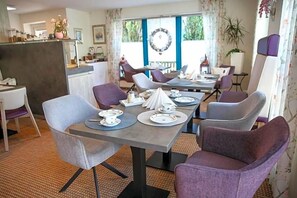 A dining area with a long table set for four, surrounded by chairs, and a counter with a vase of flowers.