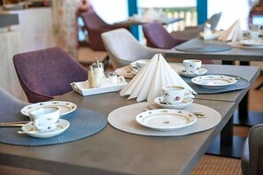 A dining table set with plates, cups, and a napkin cone in a restaurant.
