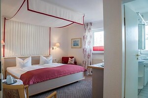 Ein Hotelzimmer mit Bett, Nachttisch, Lampe und einem Fenster mit Vorhängen.