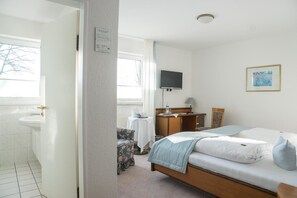 A bedroom with a bed, a desk, a chair, a television, and a window.