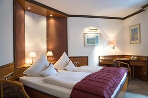 A hotel room with a double bed, two bedside lamps, a desk with a chair, and a telephone.