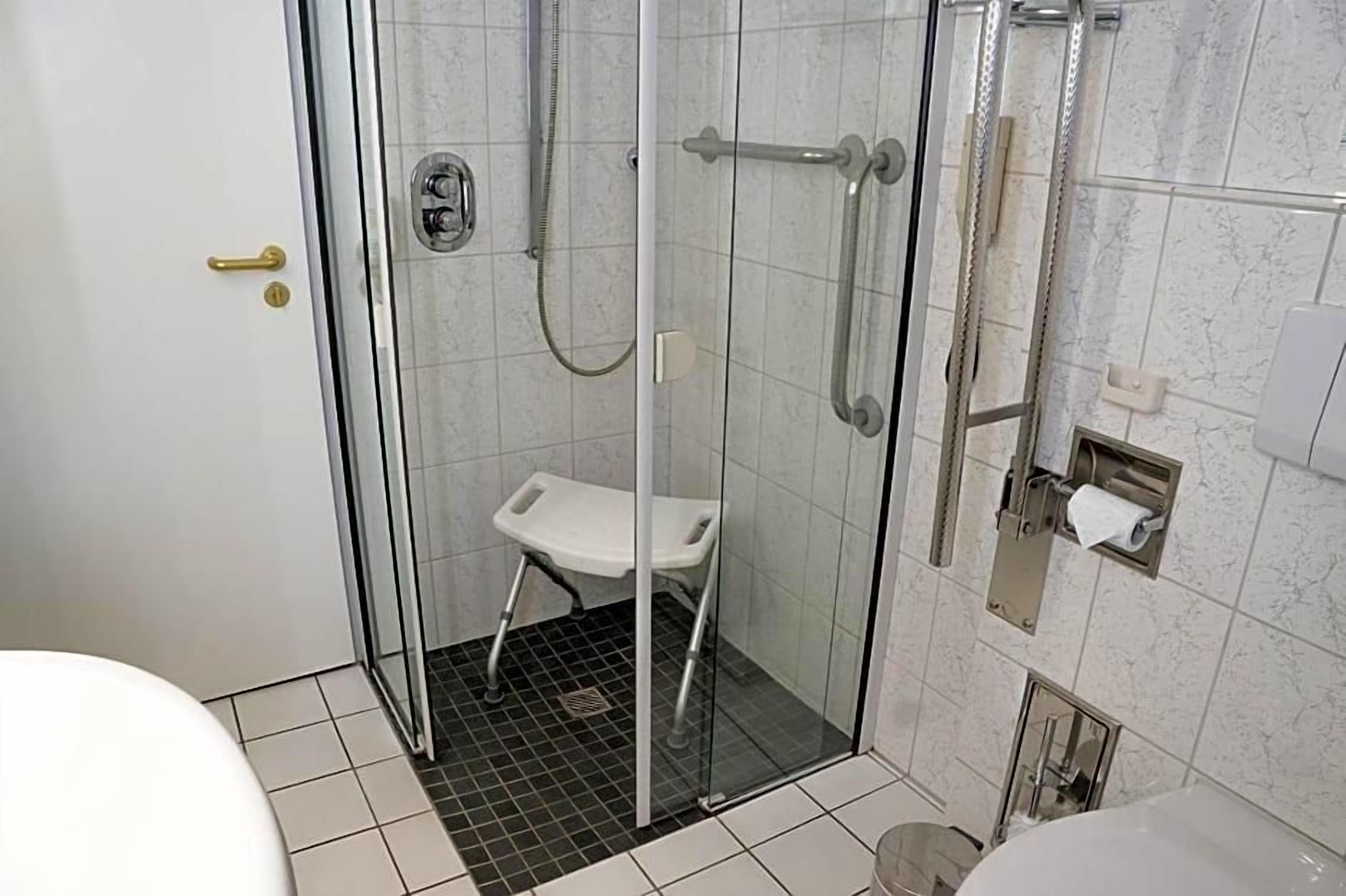Ein Duschbereich mit Glaswänden, eine weiße Sitzbank, eine Toilette und ein Handtuchspender.