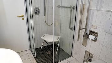 Ein Duschbereich mit Glaswänden, eine weiße Sitzbank, eine Toilette und ein Handtuchspender.