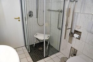 A glass-enclosed shower area with a white bench, a toilet, and a towel dispenser.