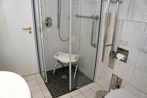 A glass-enclosed shower area with a white bench, a toilet, and a towel dispenser.