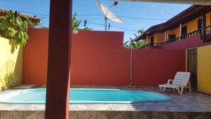 Una piscina con un muro rojo y una silla blanca.