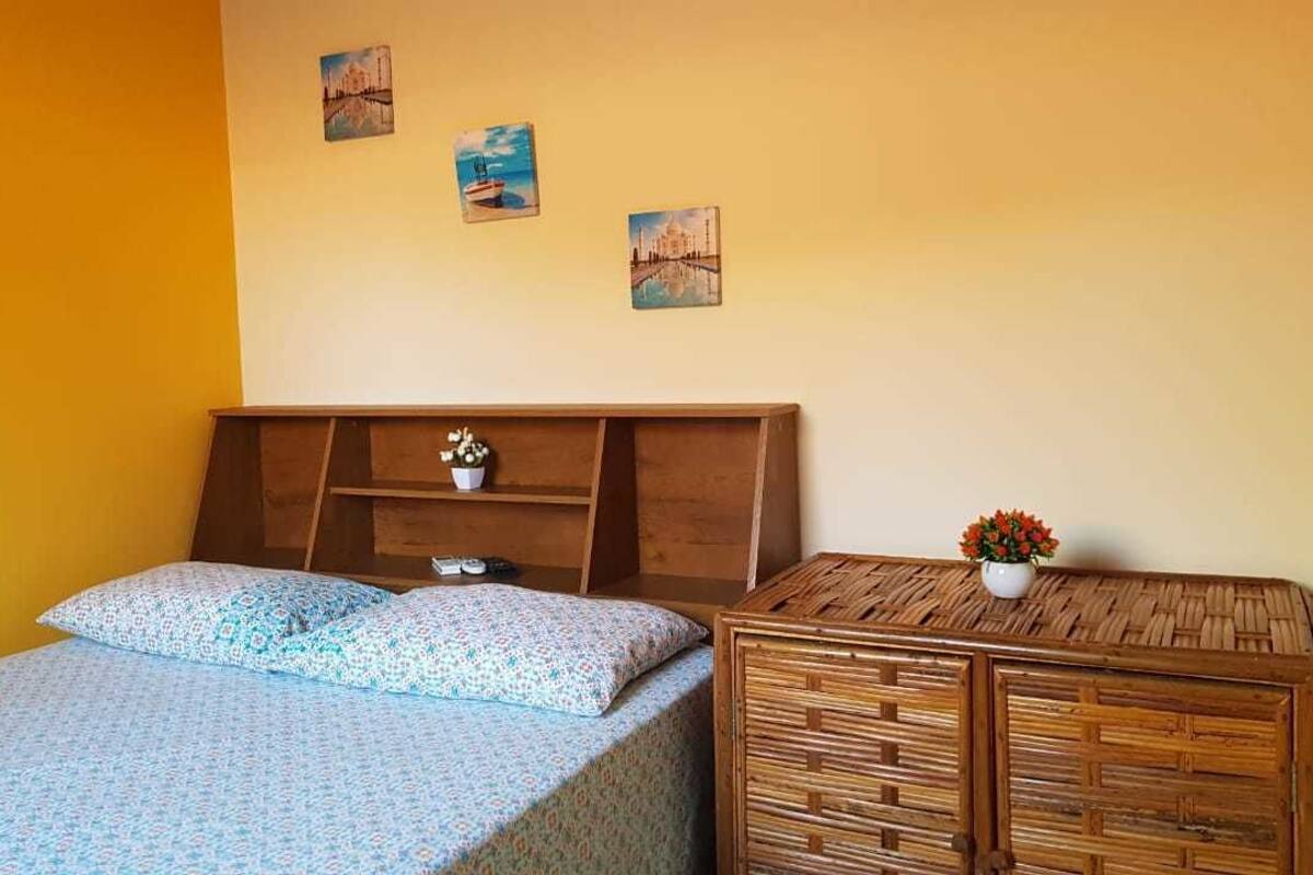 Ein Schlafzimmer mit einem Bett, einem Holznachttisch, einem kleinen Tisch mit einer Vase und Wandbildern.