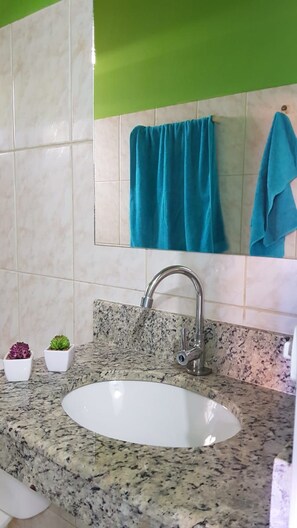 Un baño con lavamanos de encimera de granito, un espejo y una pared verde.