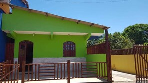 Una casa de dos pisos con fachada verde, un portón de madera y un pequeño porche.