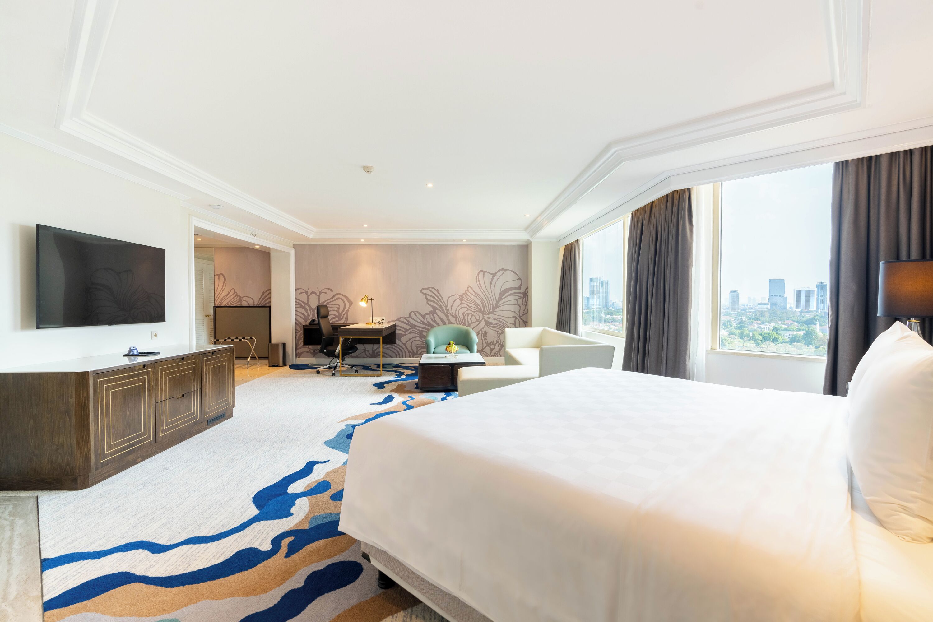 Habitación de hotel con una cama grande, un escritorio, una silla, un televisor y vistas a la ciudad.