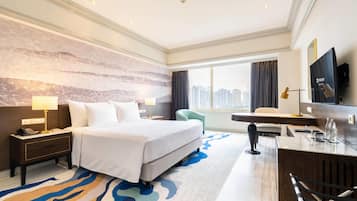 Habitación de hotel con una cama grande, un escritorio, una silla, una mesita de noche, una lámpara y vistas a la ciudad.