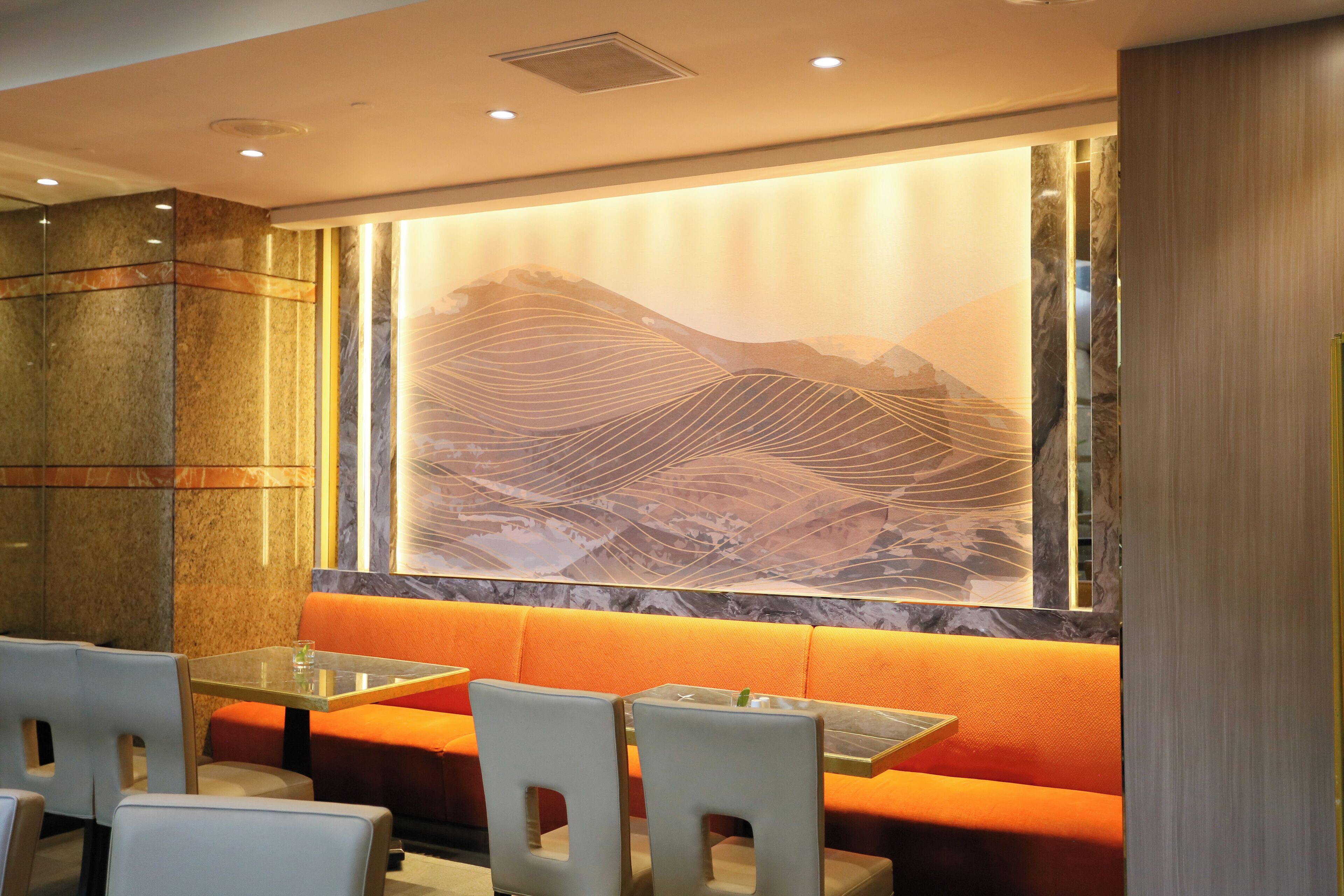Un restaurant avec un mur de marbre, des sièges orange et une grande fresque représentant des montagnes.