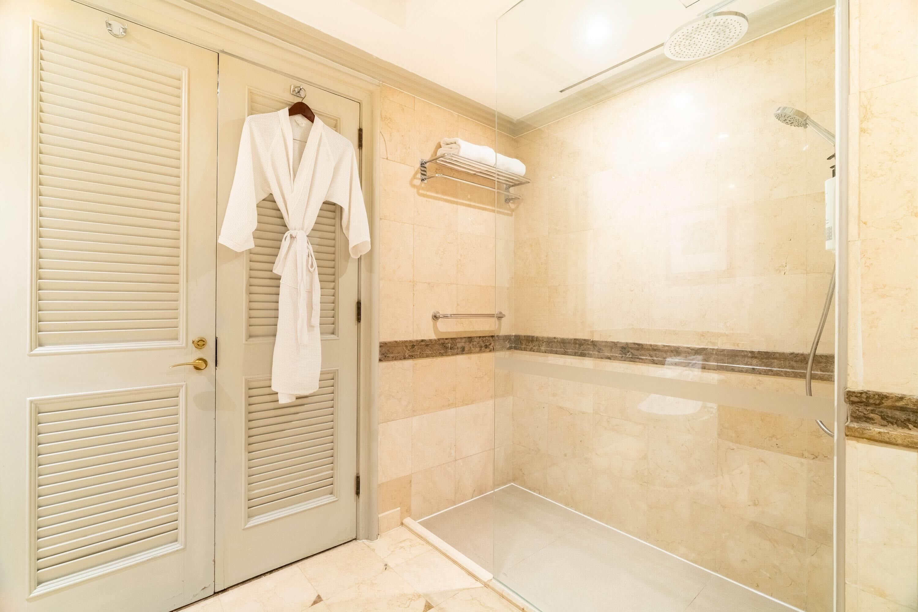 A bathroom with a glass shower enclosure, a towel rack, and a robe hanging on a door.