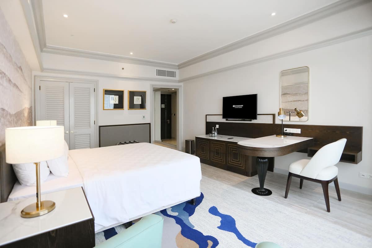 A hotel room with a bed, a desk with a chair, a television, and a bathroom door.
