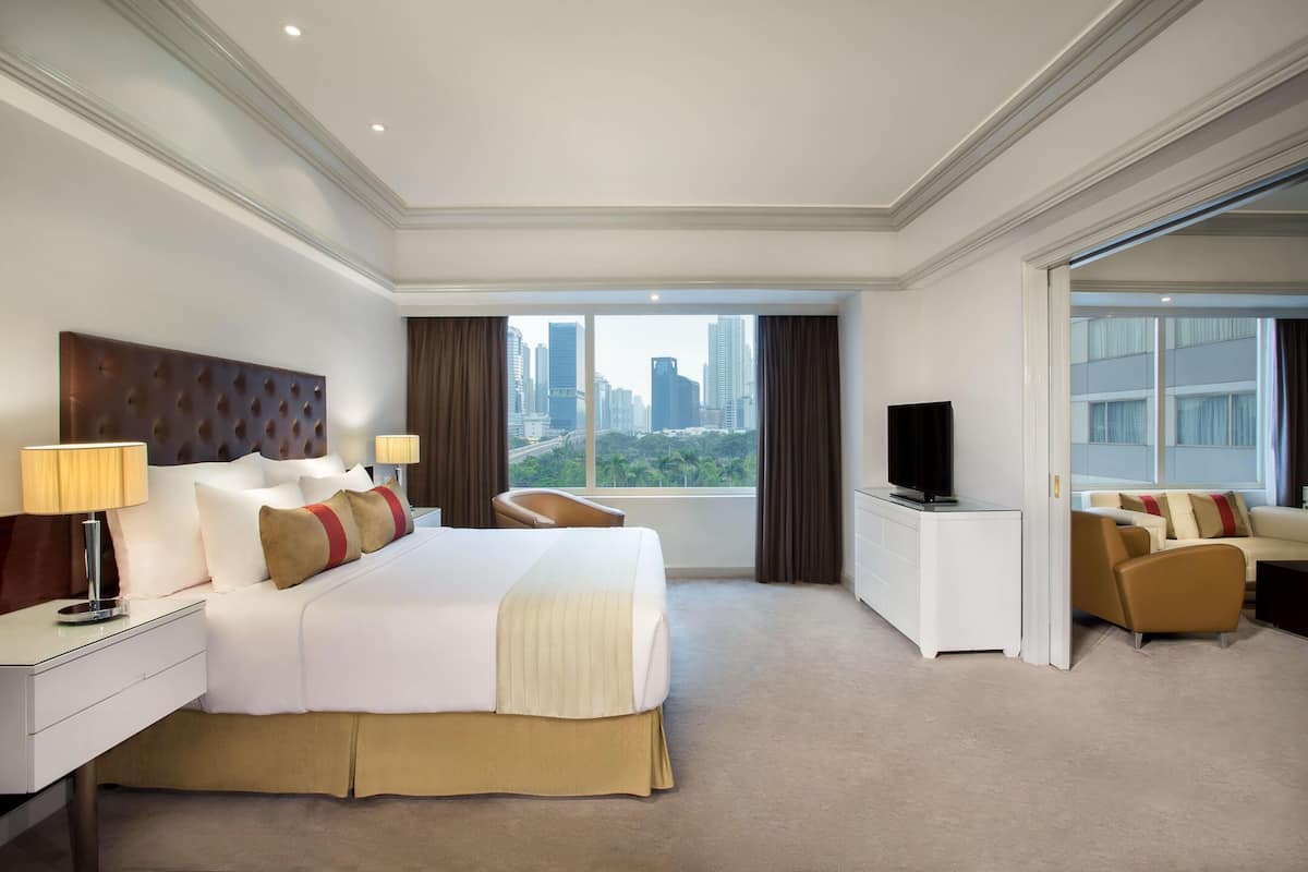 A hotel room with a large bed, a television, a desk, and a view of a cityscape.