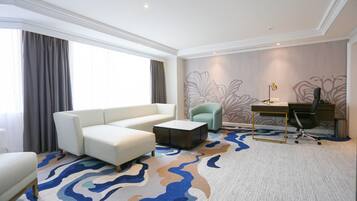 A modern hotel room with a white sofa, a small round coffee table, a desk with a chair, and a patterned carpet.