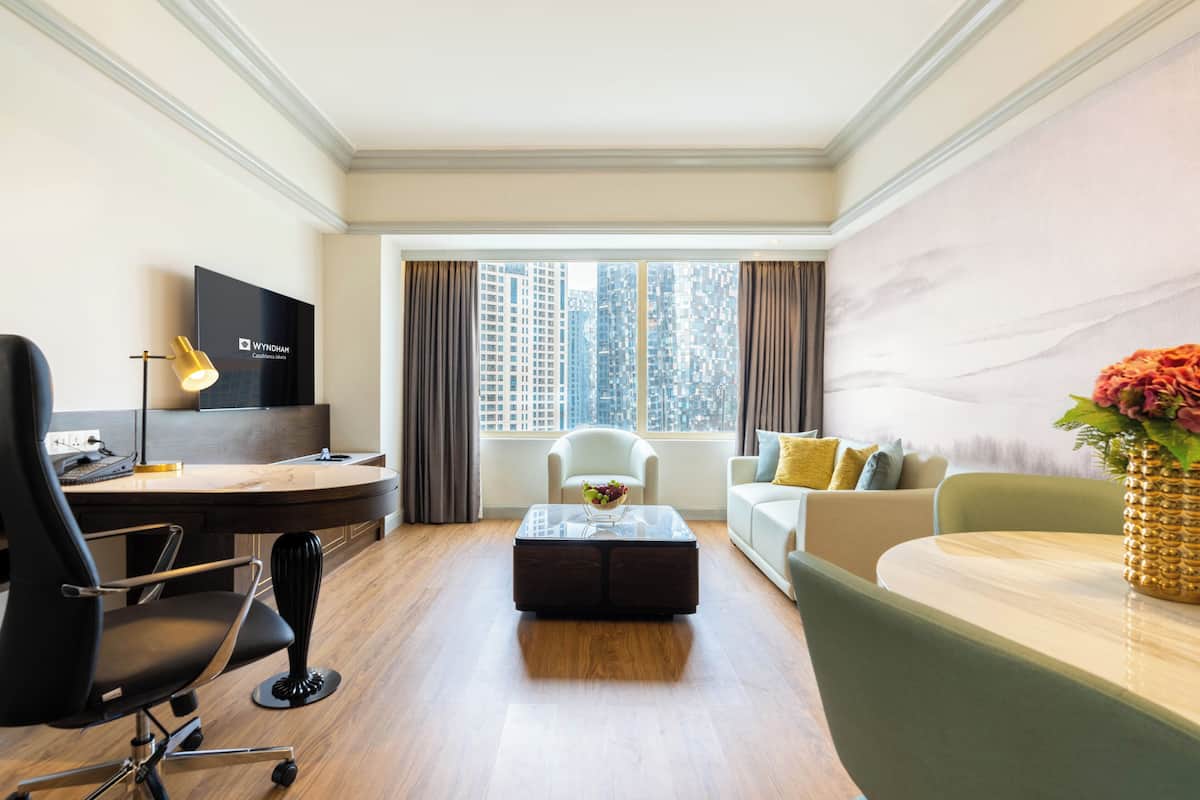 A hotel room with a desk, chair, sofa, and a large window with a city view.