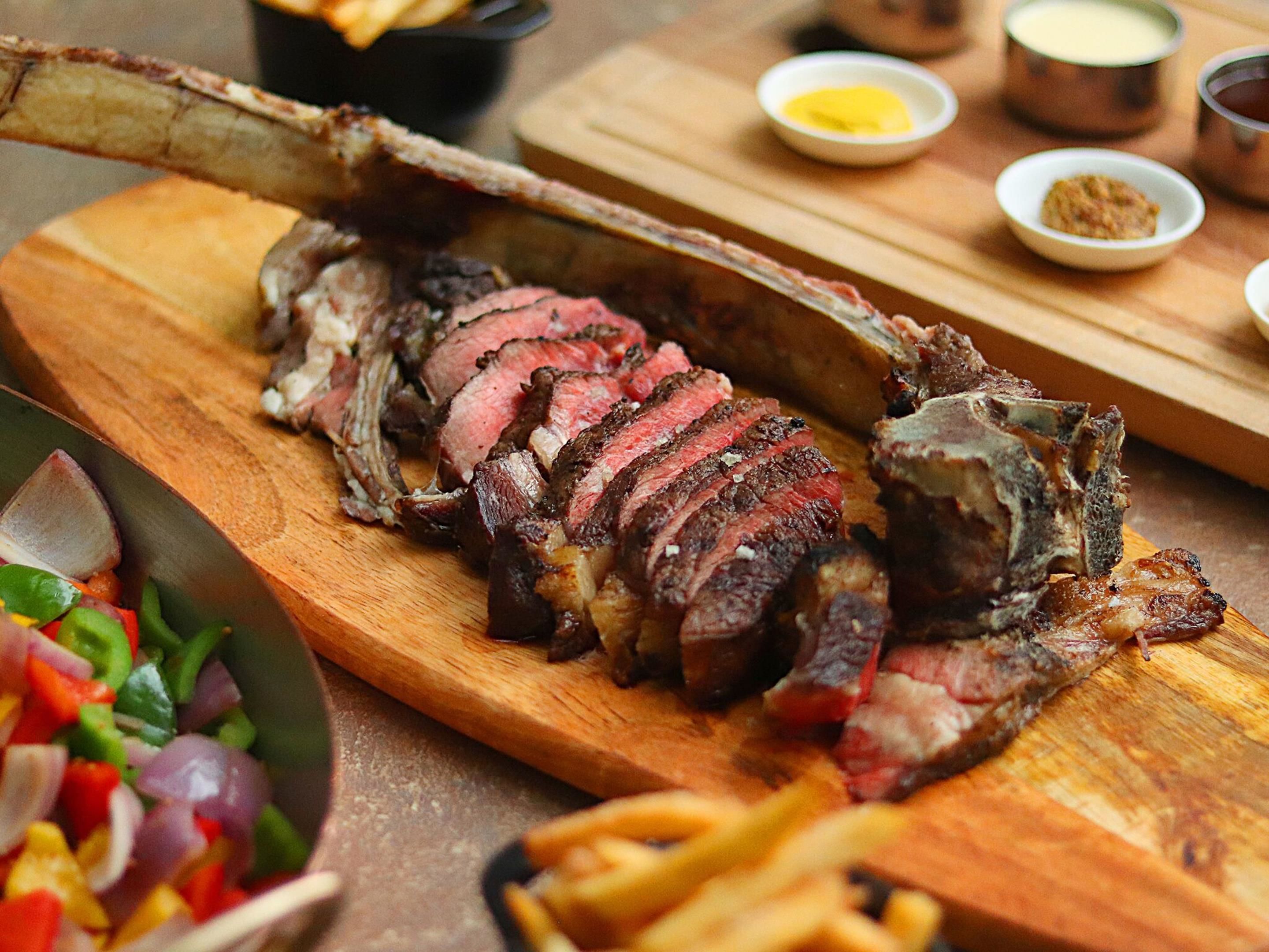 A wooden cutting board with sliced meat, possibly lamb, and a side salad.
