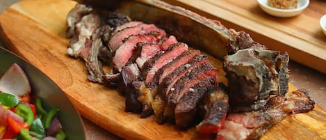 A wooden cutting board with sliced meat, possibly lamb, and a side salad.