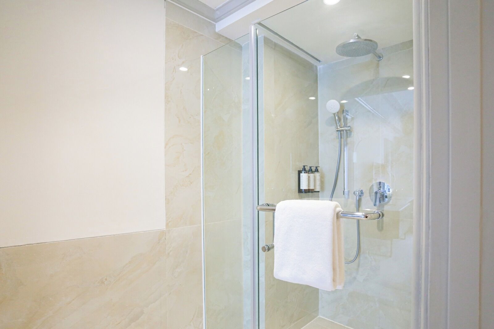 Una ducha moderna con puerta de cristal, cabezal de ducha de mano y toallero con una toalla blanca.
