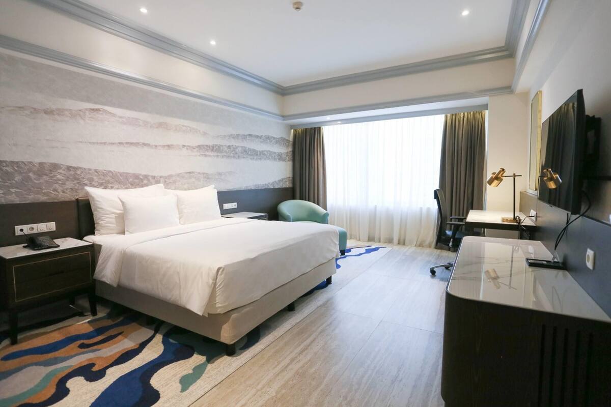 A hotel room with a bed, bedside table, desk, chair, and a TV.