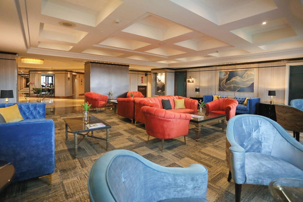 A spacious lobby with a mix of red and blue seating, a chandelier, and a large abstract painting on the wall.
