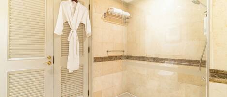 A bathroom with a glass shower enclosure, a towel rack, and a robe hanging on a door.