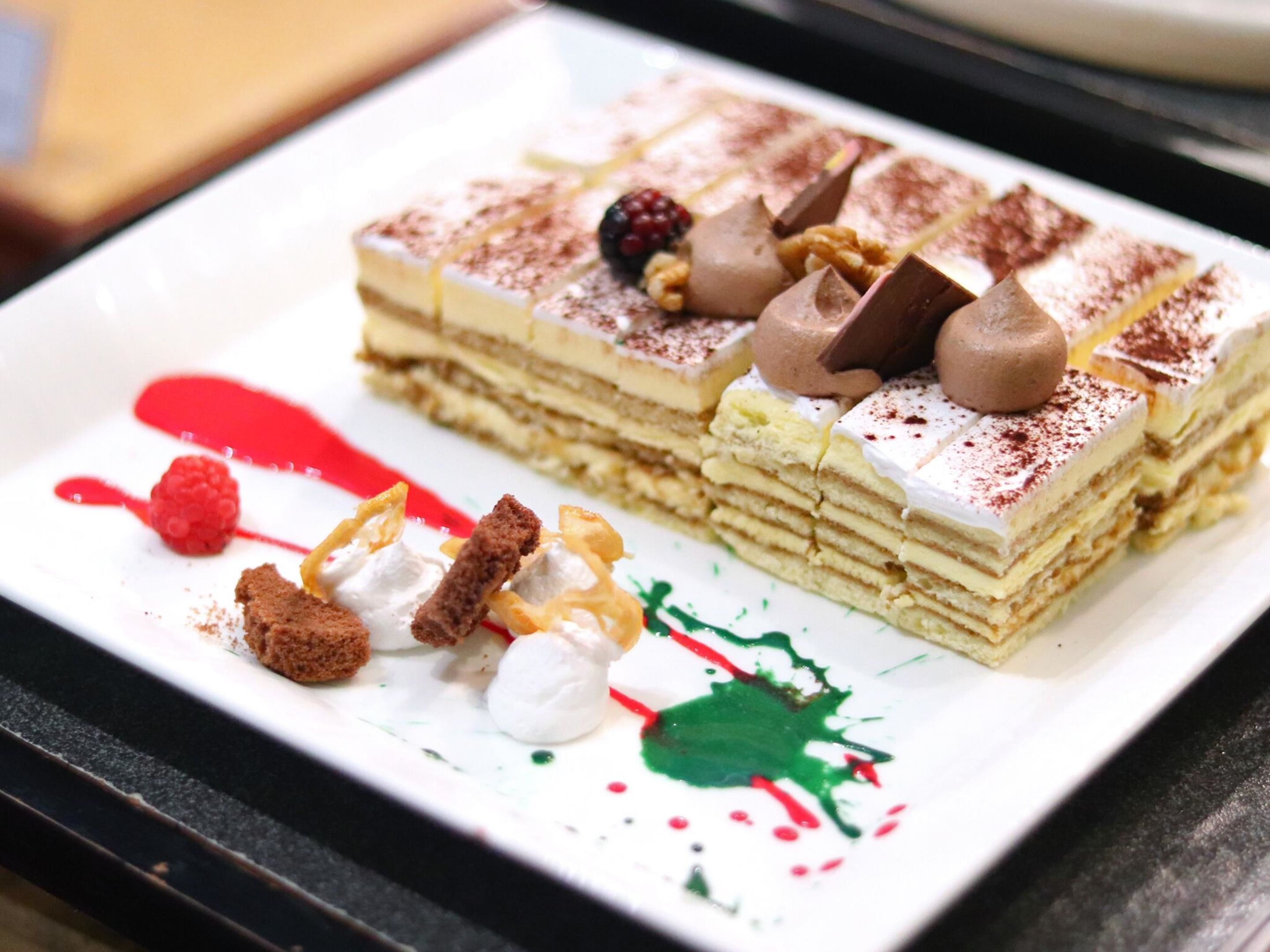 A dessert with multiple layers, topped with chocolate pieces and berries, and garnished with whipped cream and cocoa powder.