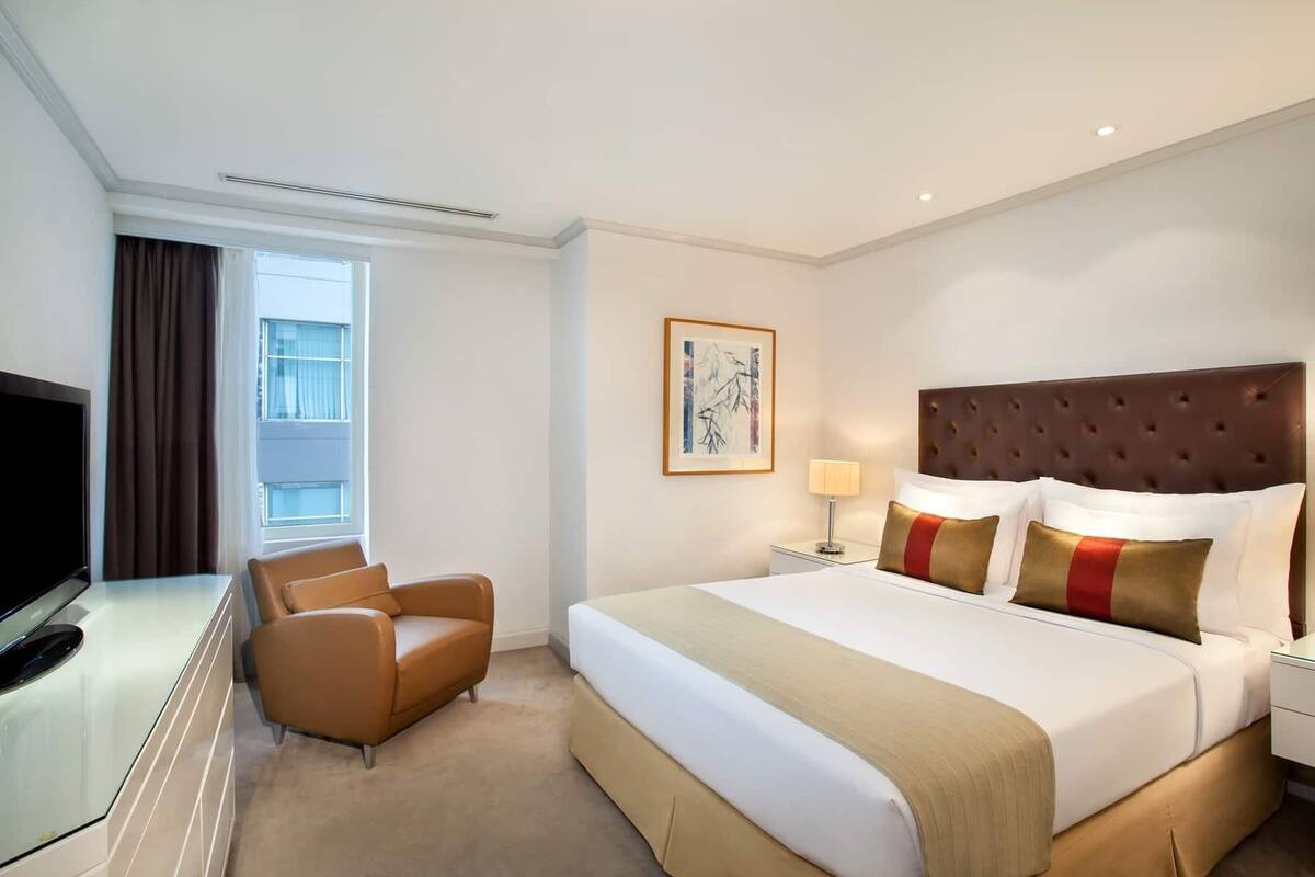 A hotel room with a bed, a TV, a chair, a nightstand, and a window.