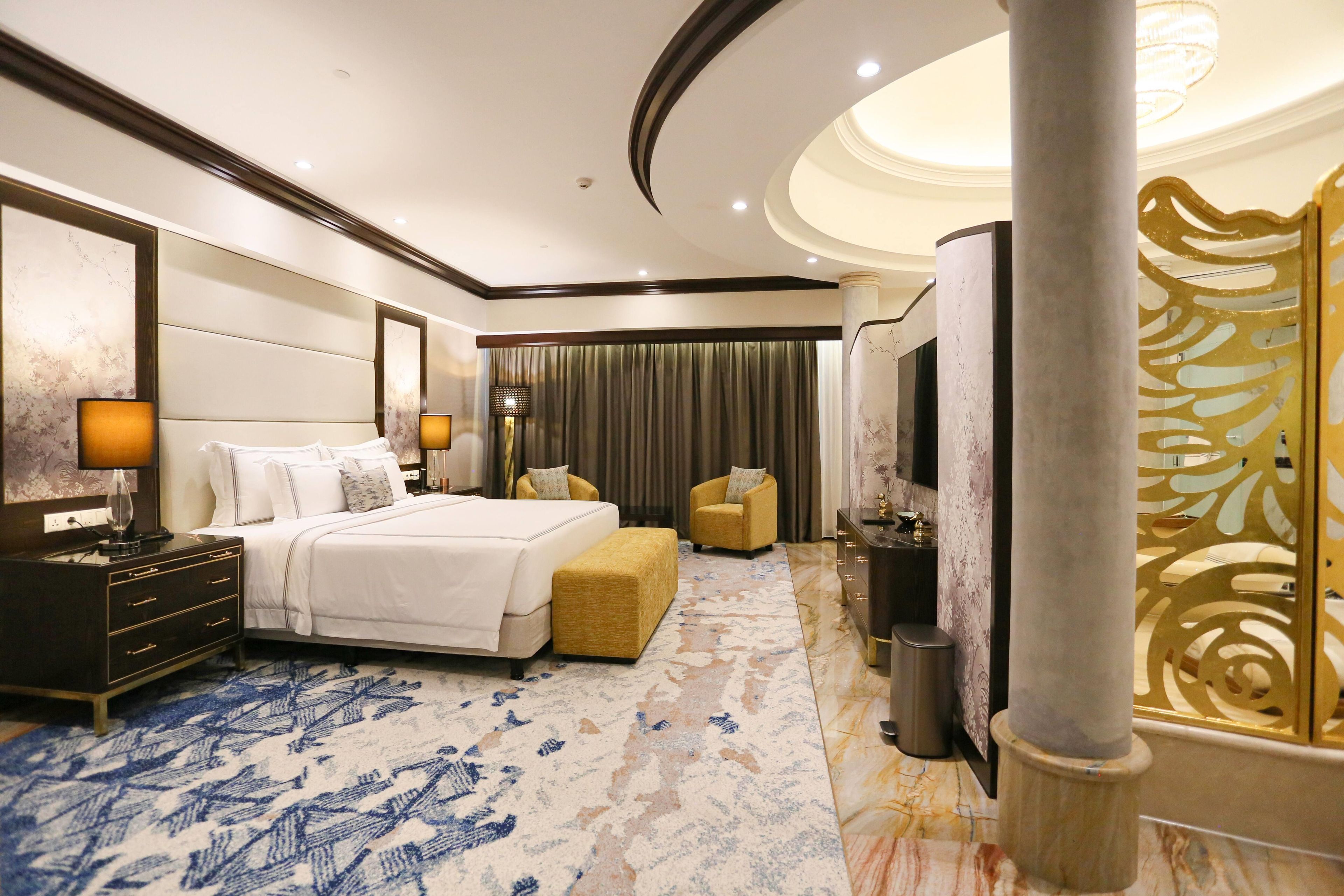 A hotel room with a large bed, a sofa, a desk, and a decorative column.