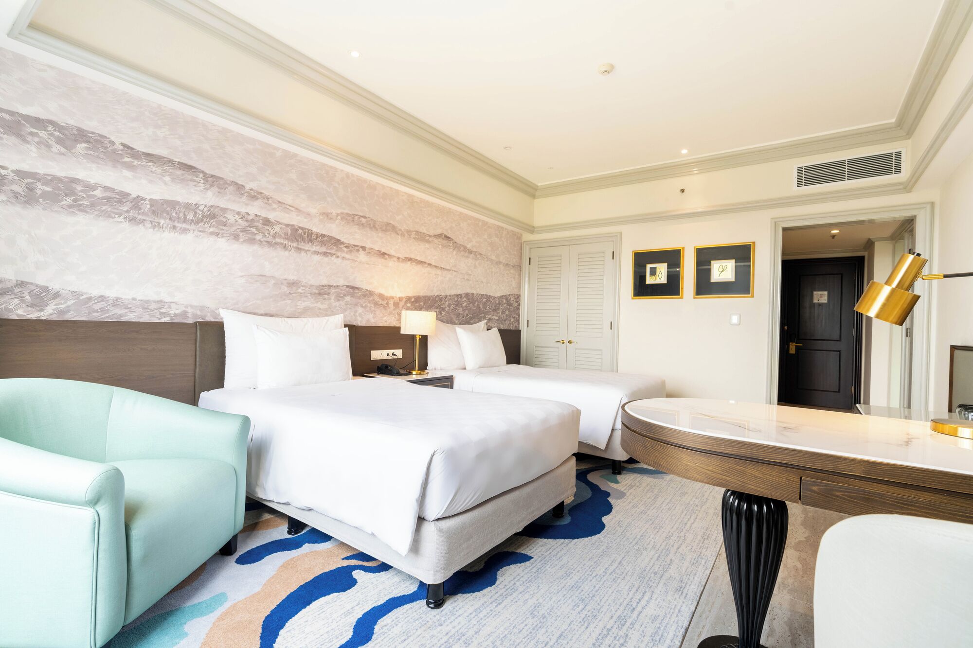 A hotel room with two beds, a desk, a chair, a bathroom, and a large mirror.
