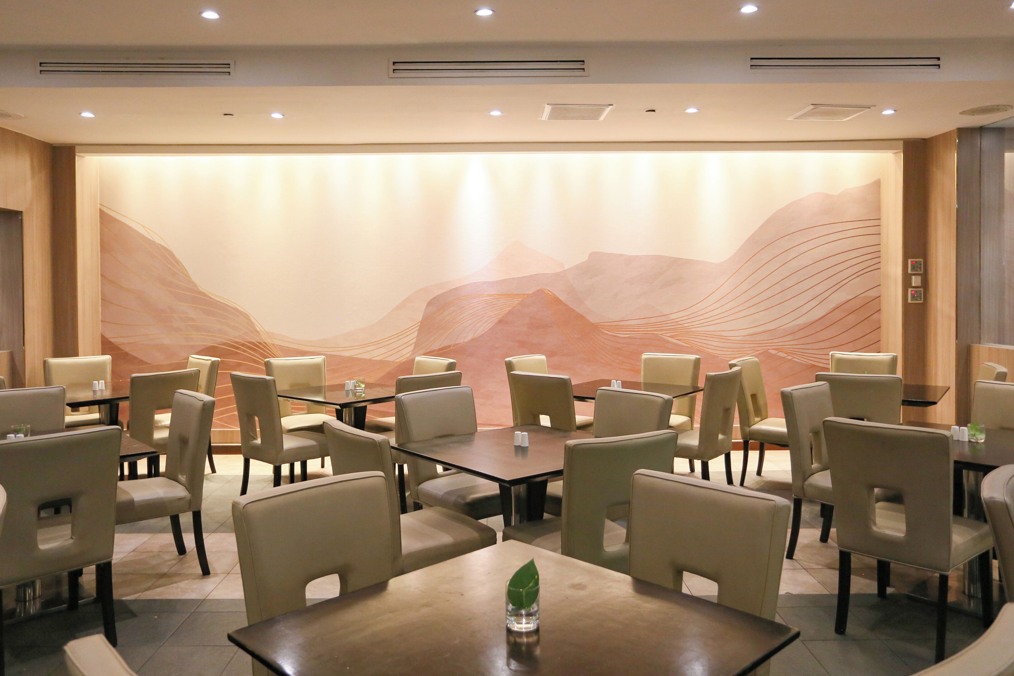 A conference room with tables and chairs, a large abstract mural on the wall, and a small plant on one table.