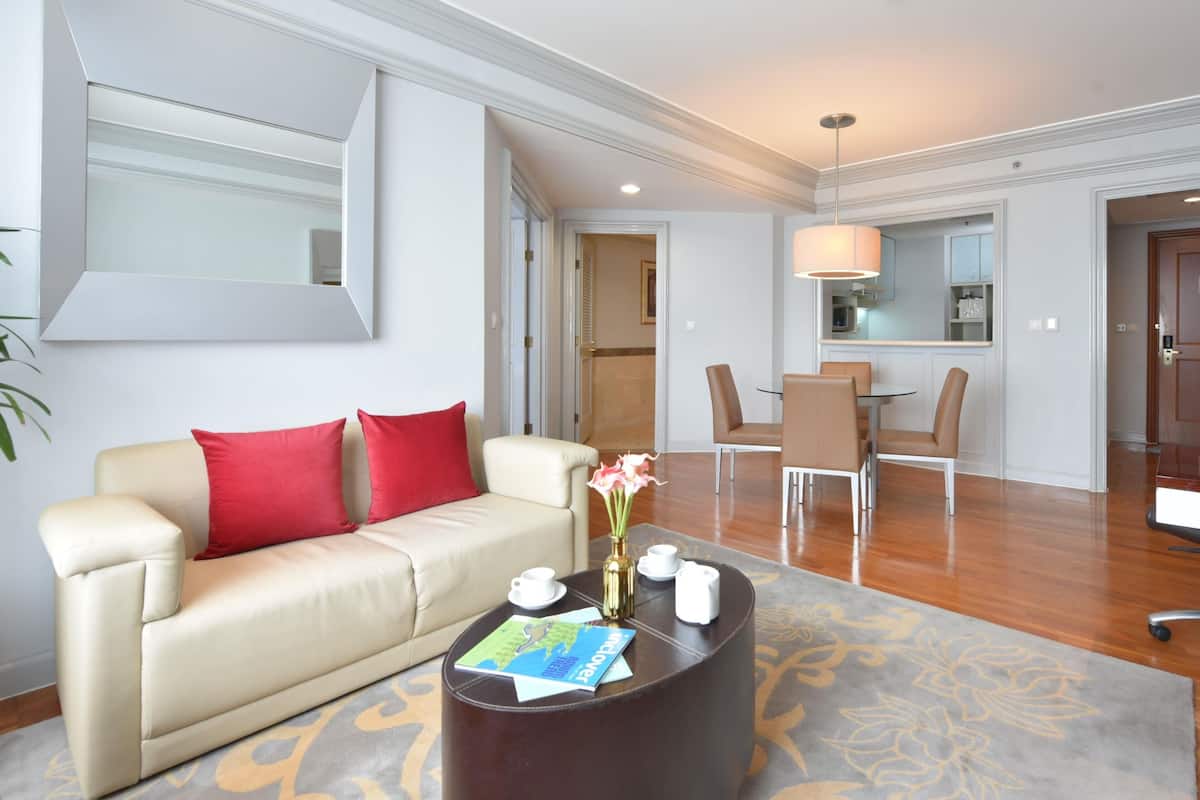 A hotel room with a sofa, coffee table, and a dining area with chairs and a table.
