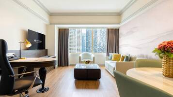 Una habitación de hotel con escritorio, silla, sofá y un ventanal con cortinas.