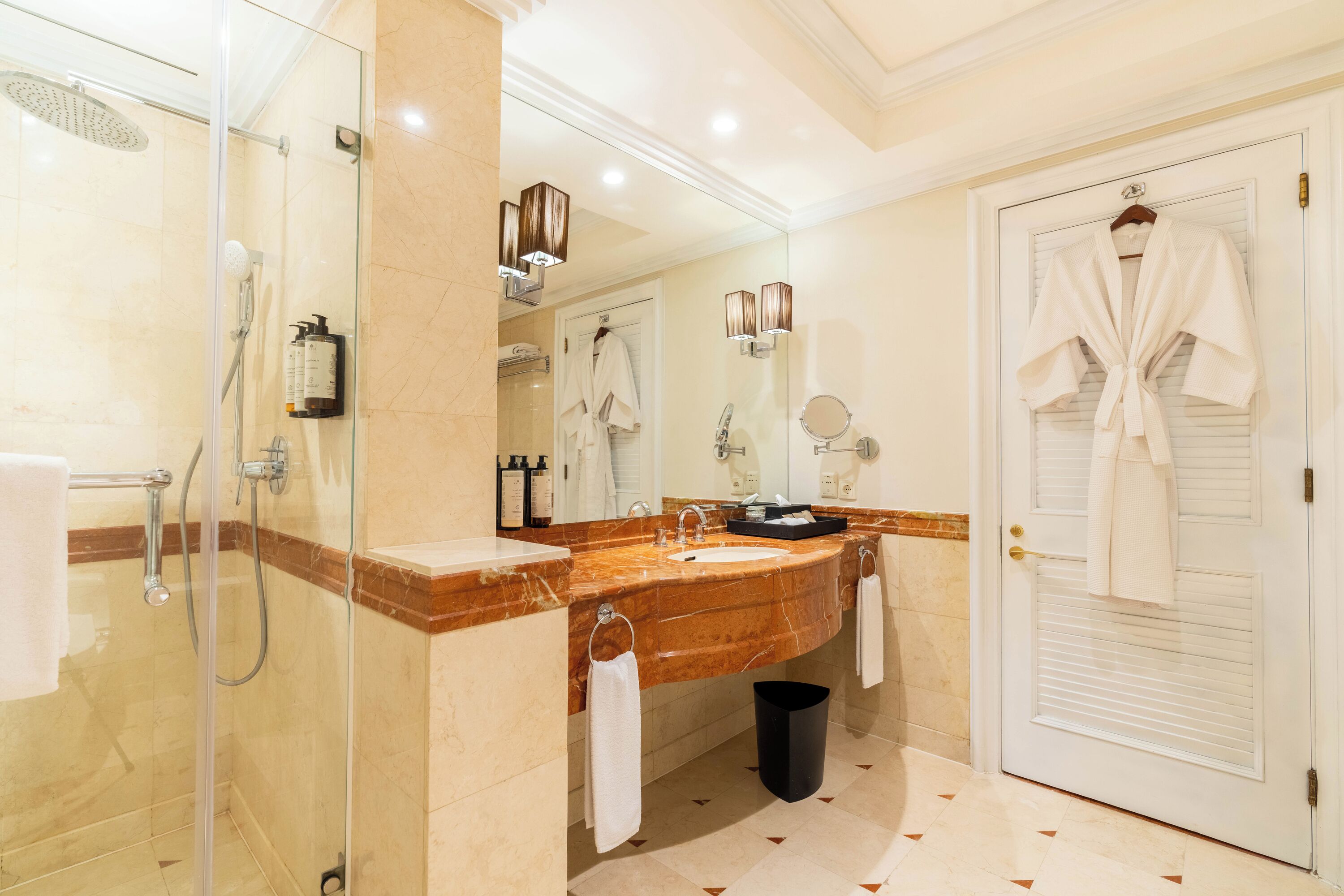 Une salle de bain avec une douche en verre, un lavabo en marbre et une porte blanche sur laquelle est accroché un peignoir.