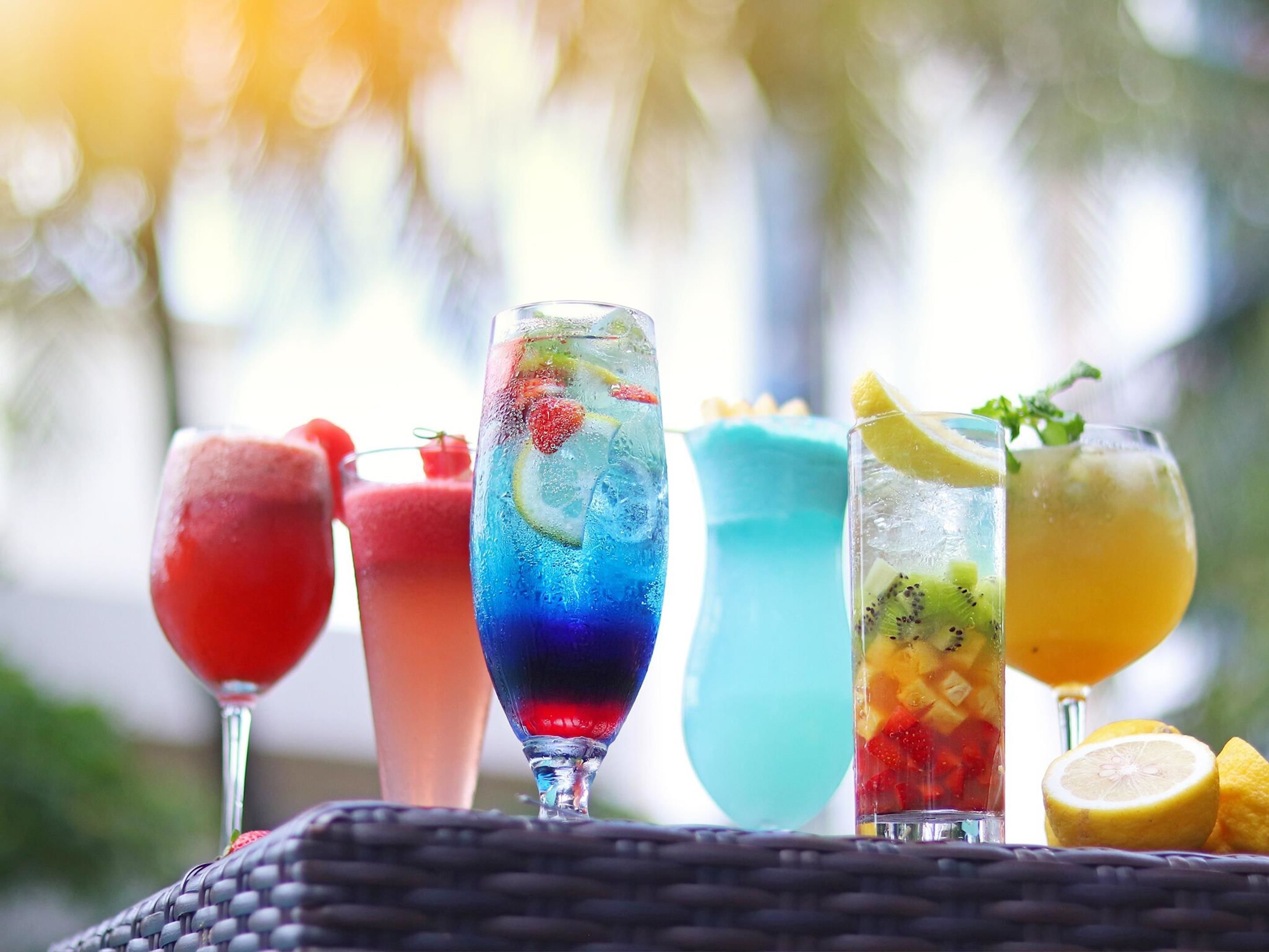 A variety of colorful drinks on a table with a wicker basket underneath.