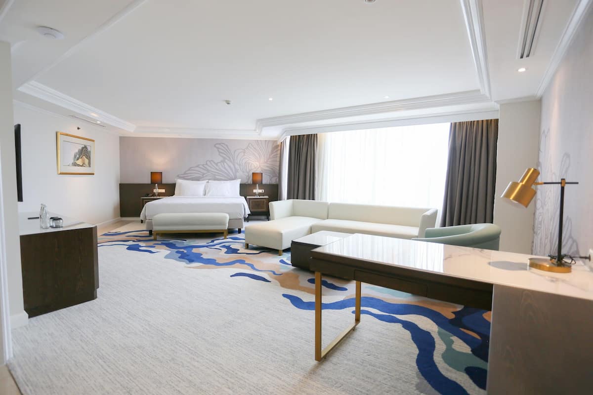 A hotel room with a bed, a sofa, a desk, and a large window.