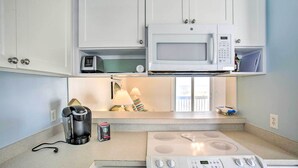 Una cocina compacta con armarios blancos, microondas, cafetera y estufa.