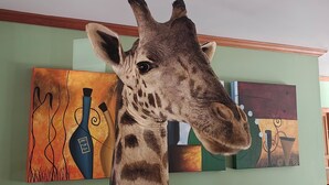 Een giraffe in een kamer met groene muren en abstracte schilderijen.