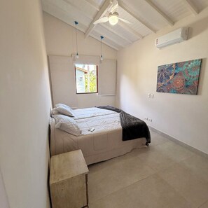 A bedroom with a bed, a ceiling fan, a window, an air conditioner, and a wall-mounted artwork. - New Year's Eve 2026 - house + housekeeping services. Convenience and comfort (São Sebastião)