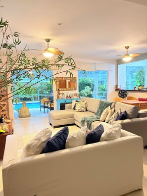 A modern living room with a sectional sofa, a dining area, and a view of a swimming pool.