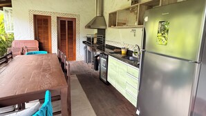 A kitchen with a stainless steel refrigerator, wooden dining table, and chairs with blue cushions. - New Year's Eve 2026 - house + housekeeping services. Convenience and comfort (São Sebastião)