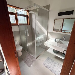 Een moderne badkamer met een douchecabine van glas, een toilet, een wastafel en een spiegel.