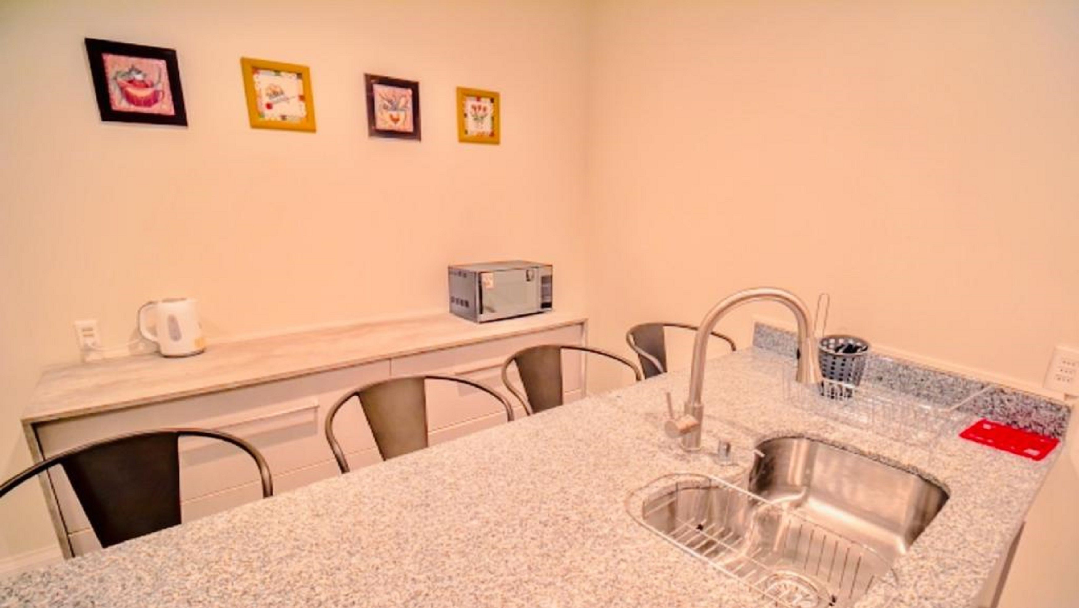 A compact kitchen with a granite countertop, a sink, and a toaster. There are four chairs around the table, and three framed pictures on the wall.