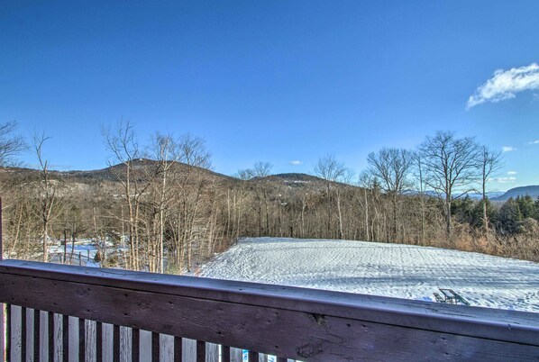 A snow-covered landscape with a wooden deck and a view of a hilly area with trees.