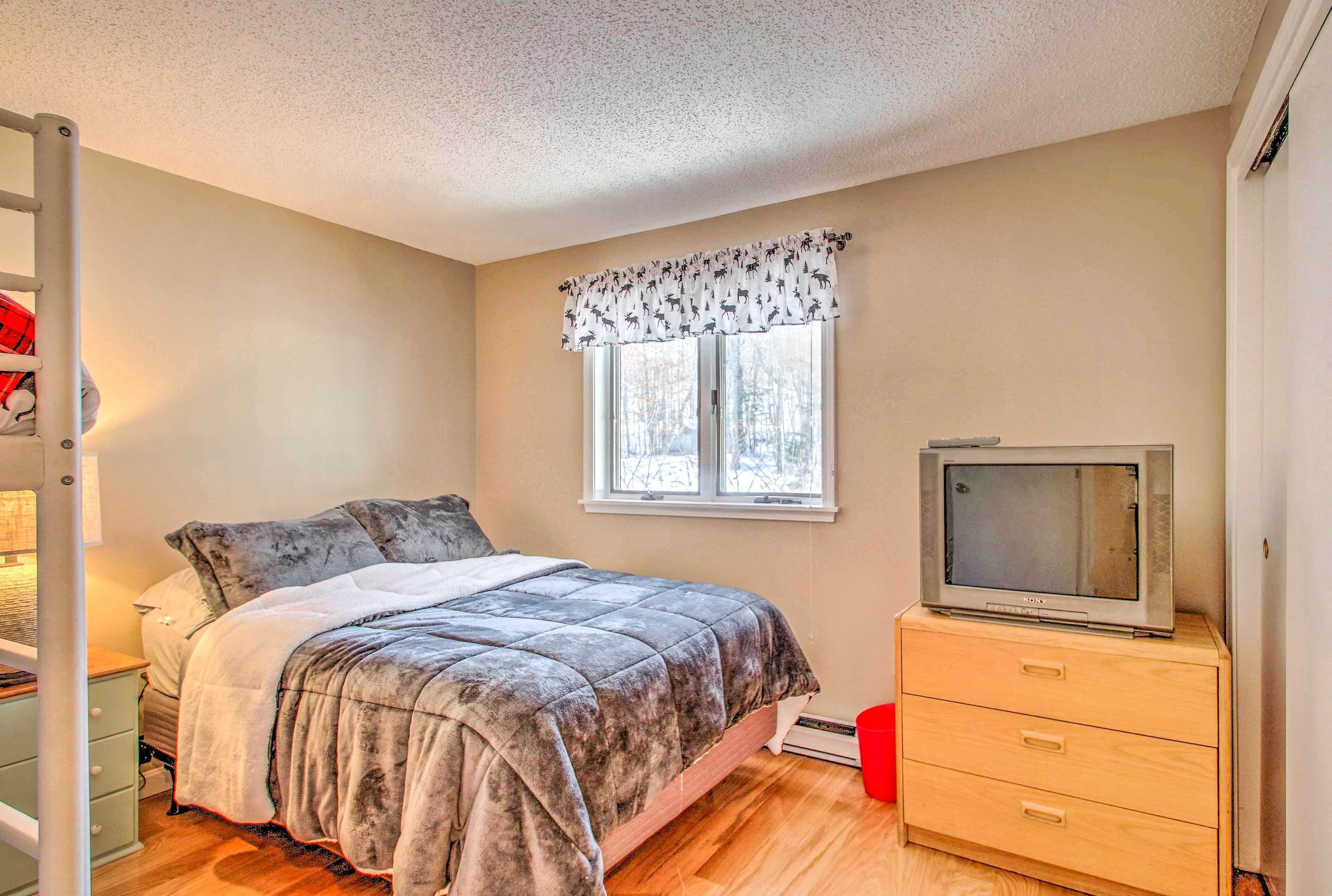 Une chambre à coucher avec un lit, une commode, un téléviseur et une fenêtre avec un rideau.