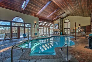 An indoor swimming pool with a wooden ceiling, lounge chairs, and a stone wall.
