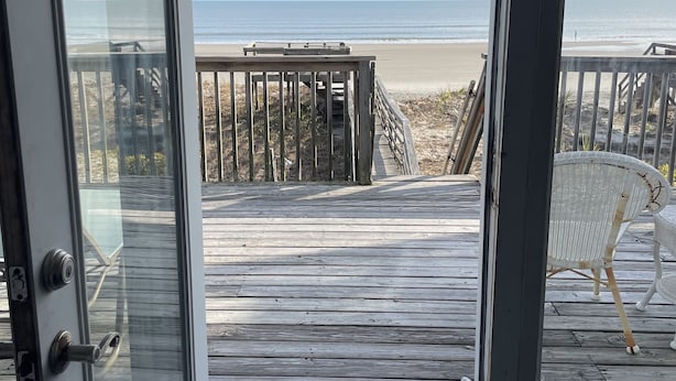 On peut admirer la plage depuis une porte qui donne sur une terrasse en bois menant à la plage.